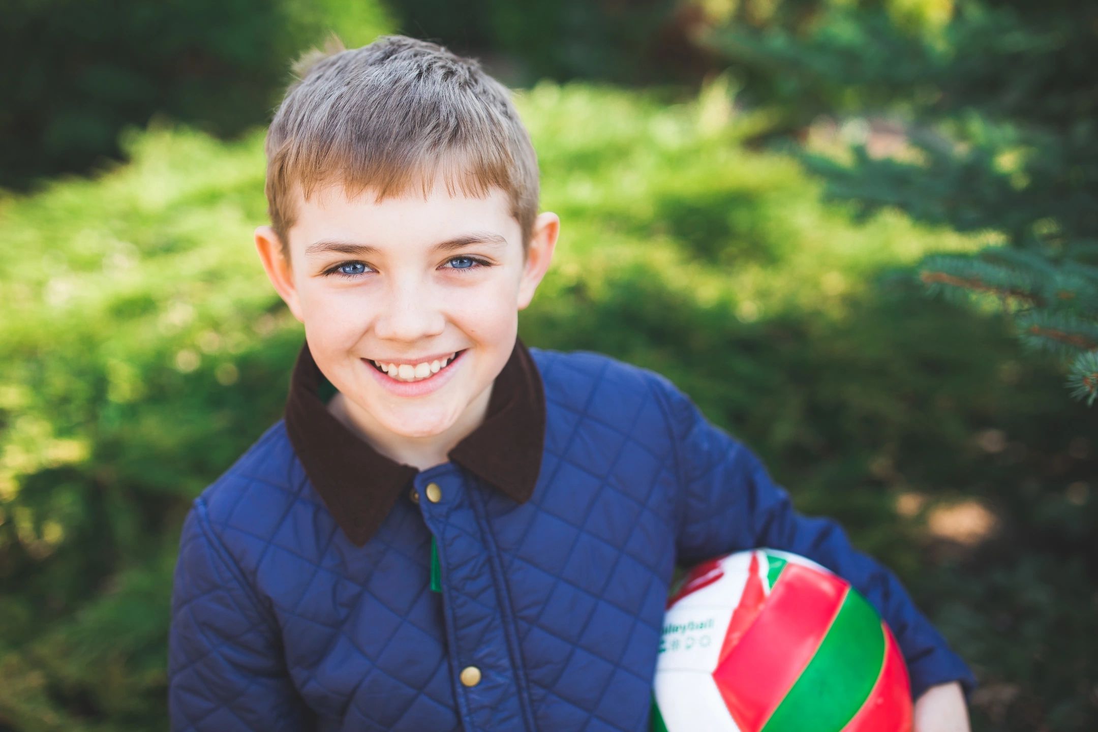 Smiling boy holding a volleyball outdoors.