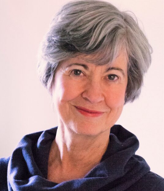 Smiling elderly woman with short gray hair and a blue scarf.