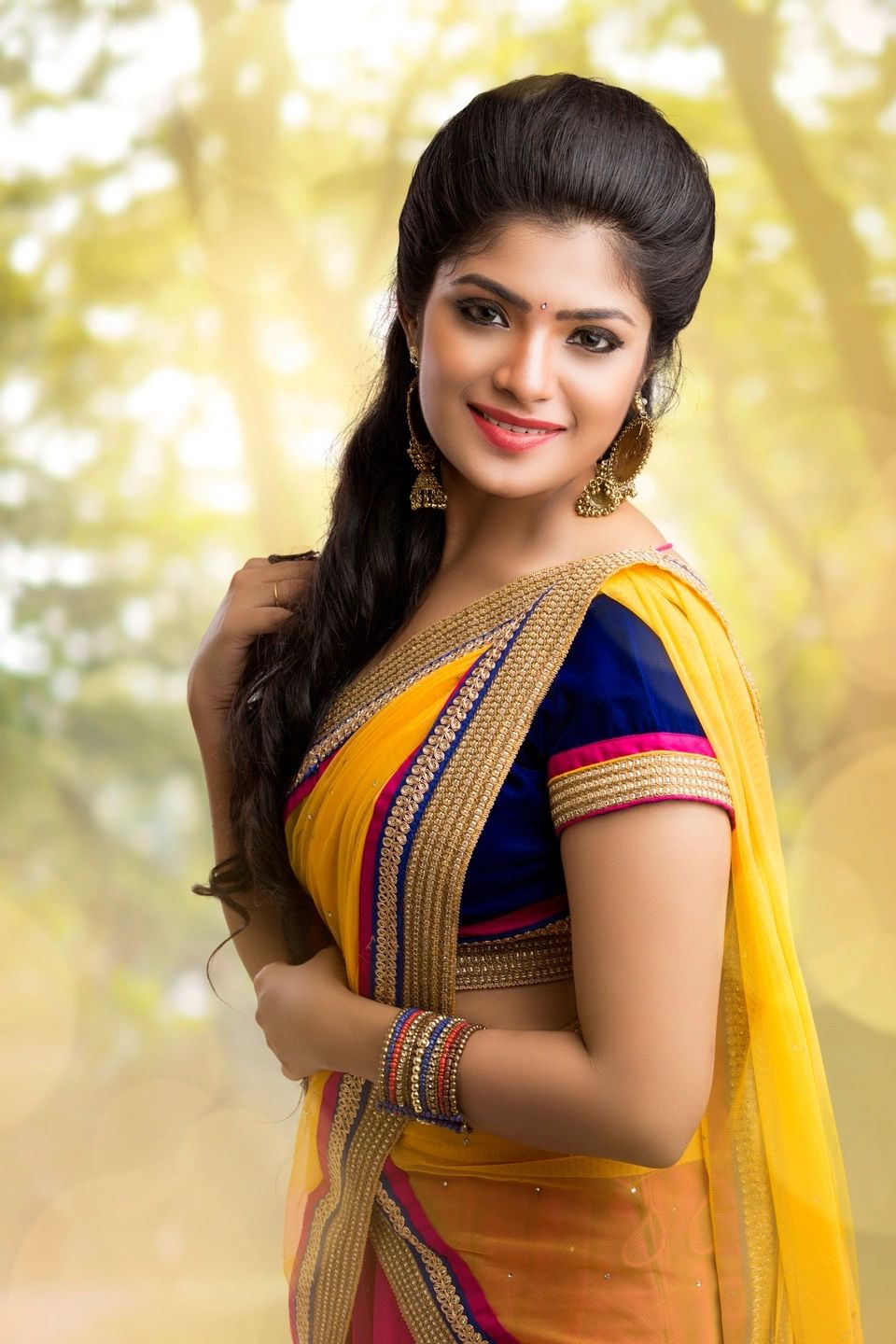 A woman smiling, dressed in a colorful traditional saree with bangles.