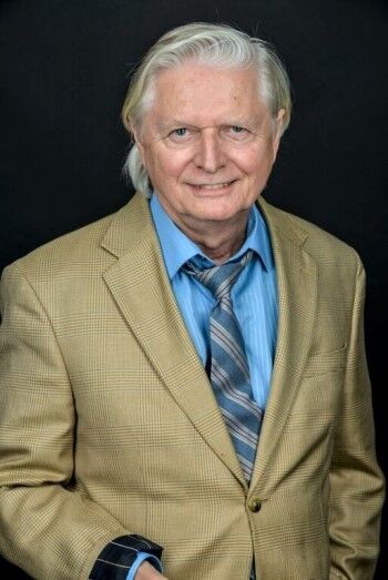 Smiling elderly man in tan blazer and blue shirt.